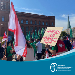 Foto der Demo mit Schild "Menschen vor Haushaltspläne" im Vordergrund